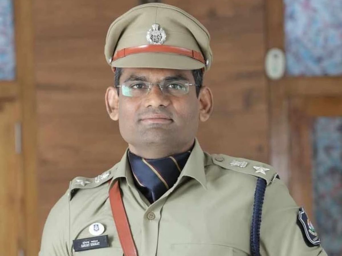 Formal portrait of Sanjay Kharat in police uniform with peaked cap, lanyard and rank insignia, indoors against a wooden panelled wall.