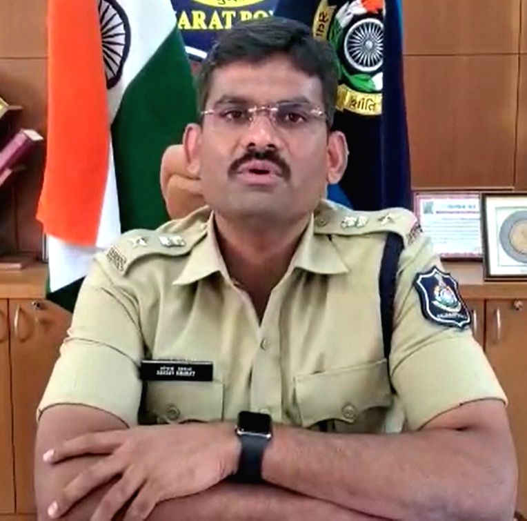Sanjay Kharat seated at his office desk addressing a camera, with the national flag and the Gujarat Police emblem on the wall behind him.